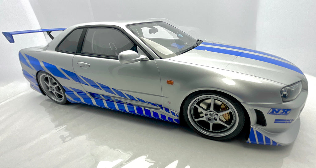 Vista laterale ribassata del modellino Nissan Skyline R34 GT-R argento e blu.