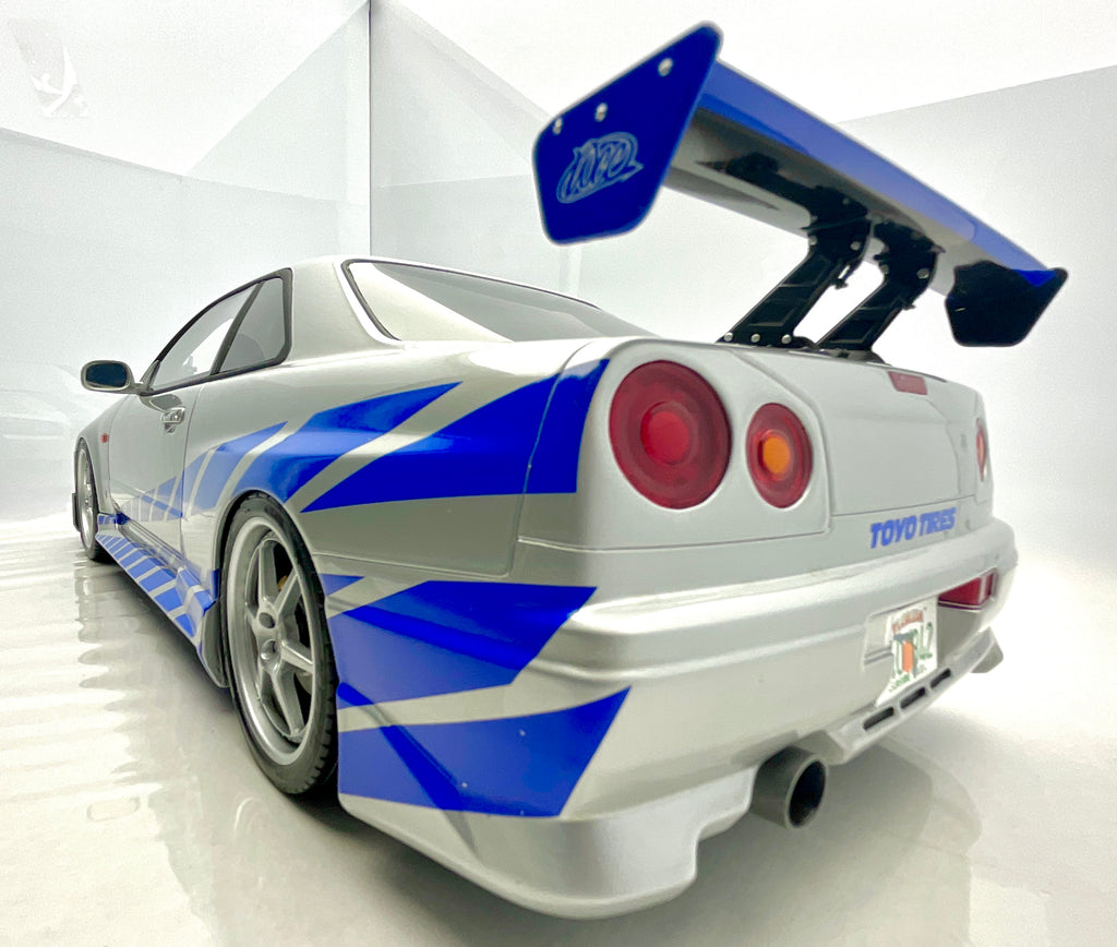  Vista posteriore a tre quarti della Nissan Skyline R34 argento e blu, con alettone e fanali tondi