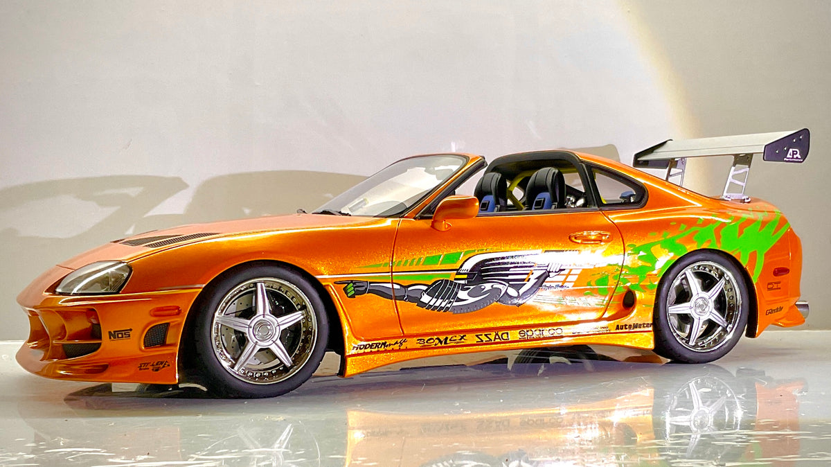 Foto laterale: Toyota Supra Fast & Furious Kyosho 1:12, vista laterale con livrea arancione, grafiche verdi, cerchi a cinque razze e alettone